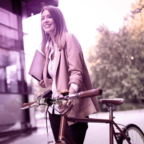 Woman holding a laptop and smiling while pushing a bicycle.