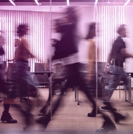 Blurred image from behind glass of multiple people walking through an office.
