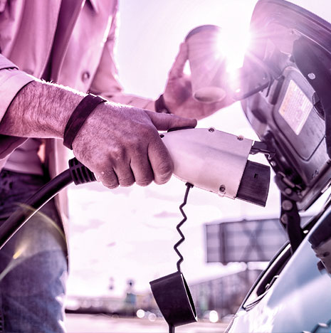 Man connecting charger to electric car with right hand, while holding a coffee in left hand.