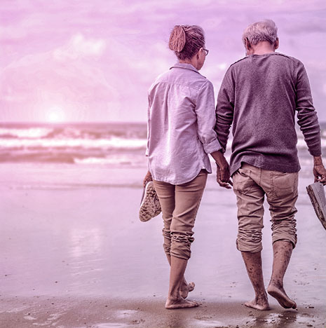 Retired couple walking on the beach holding hands.