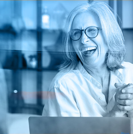 Lady with glasses laughing and holding her hands together with joy.
